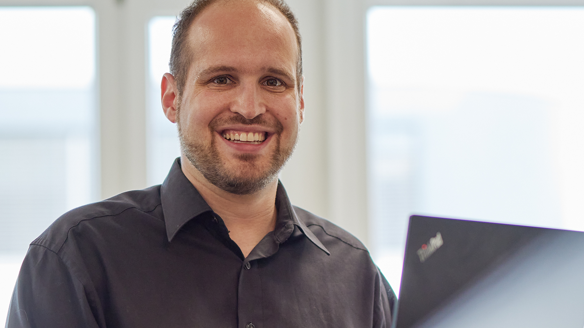 Adrian Aellig mit schwarzem Hemd vor Laptop