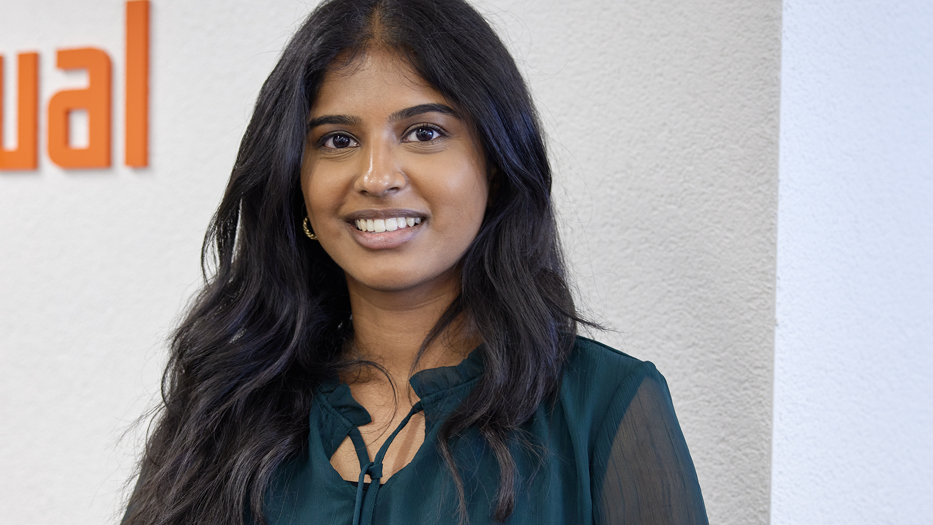 Migana Paramsothinathan mit dunkelgrüner Bluse vor weisser Wand mit angeschnittenem iqual Logo