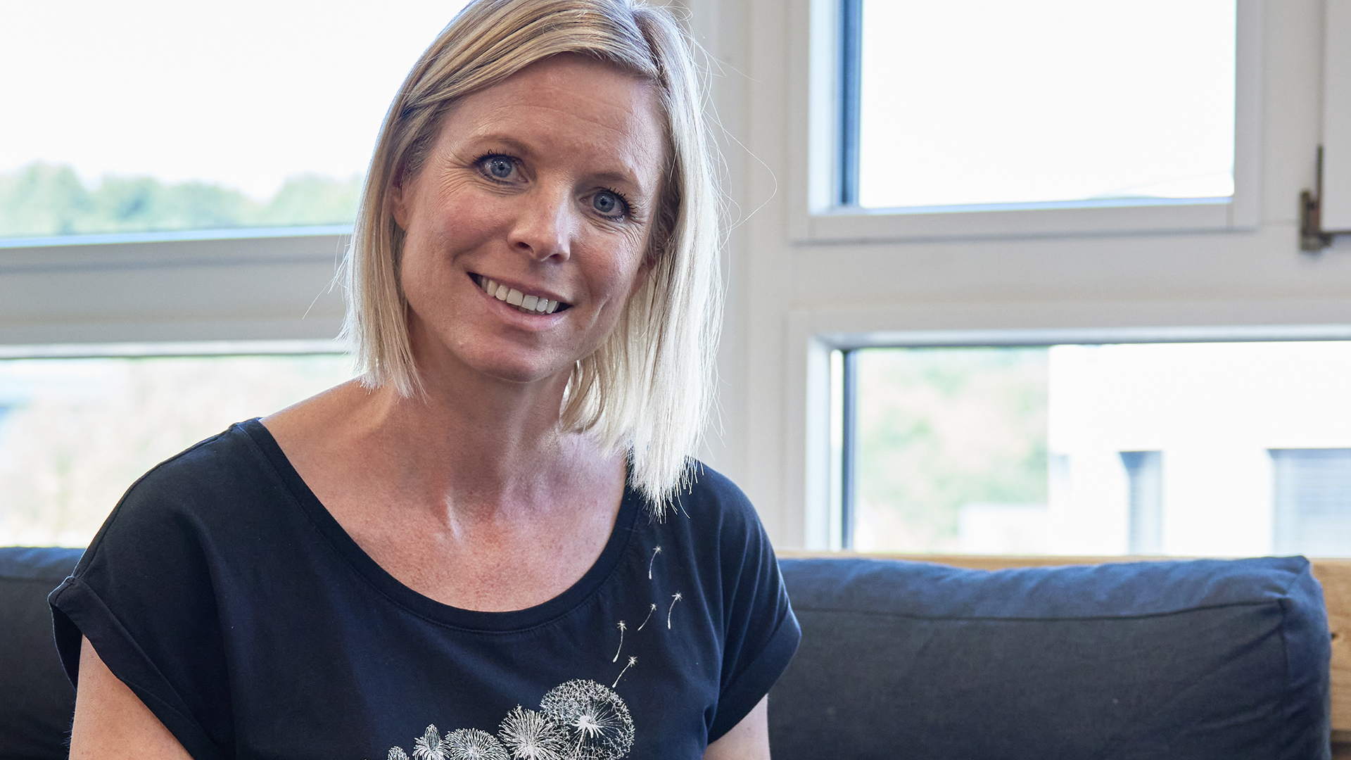 Corina Fuhrer mit schwarzem T-Shirt auf Sofa sitzend vor Fenster