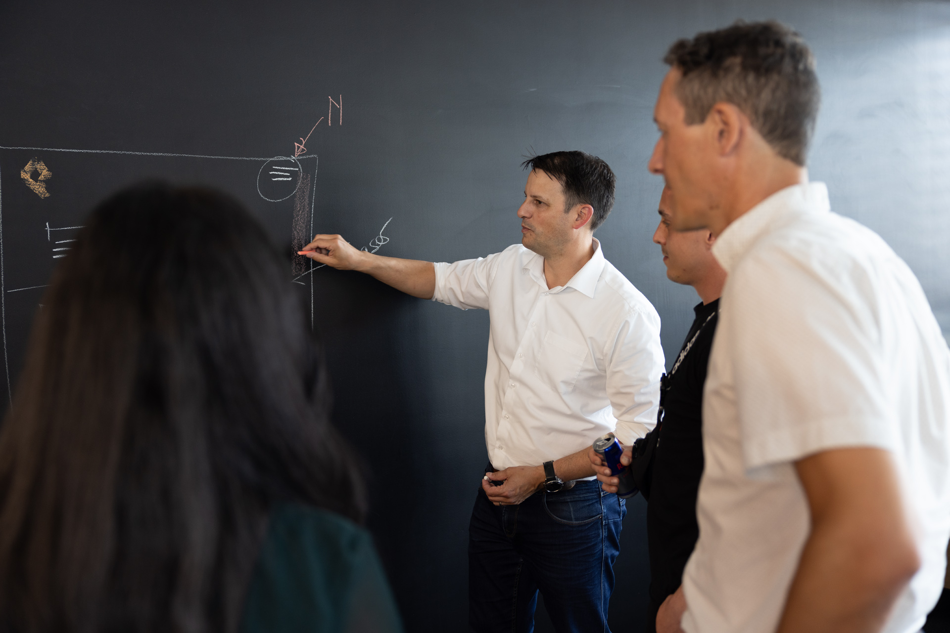 Luc an der erklärt eine Grafik an der schwarzen Wand