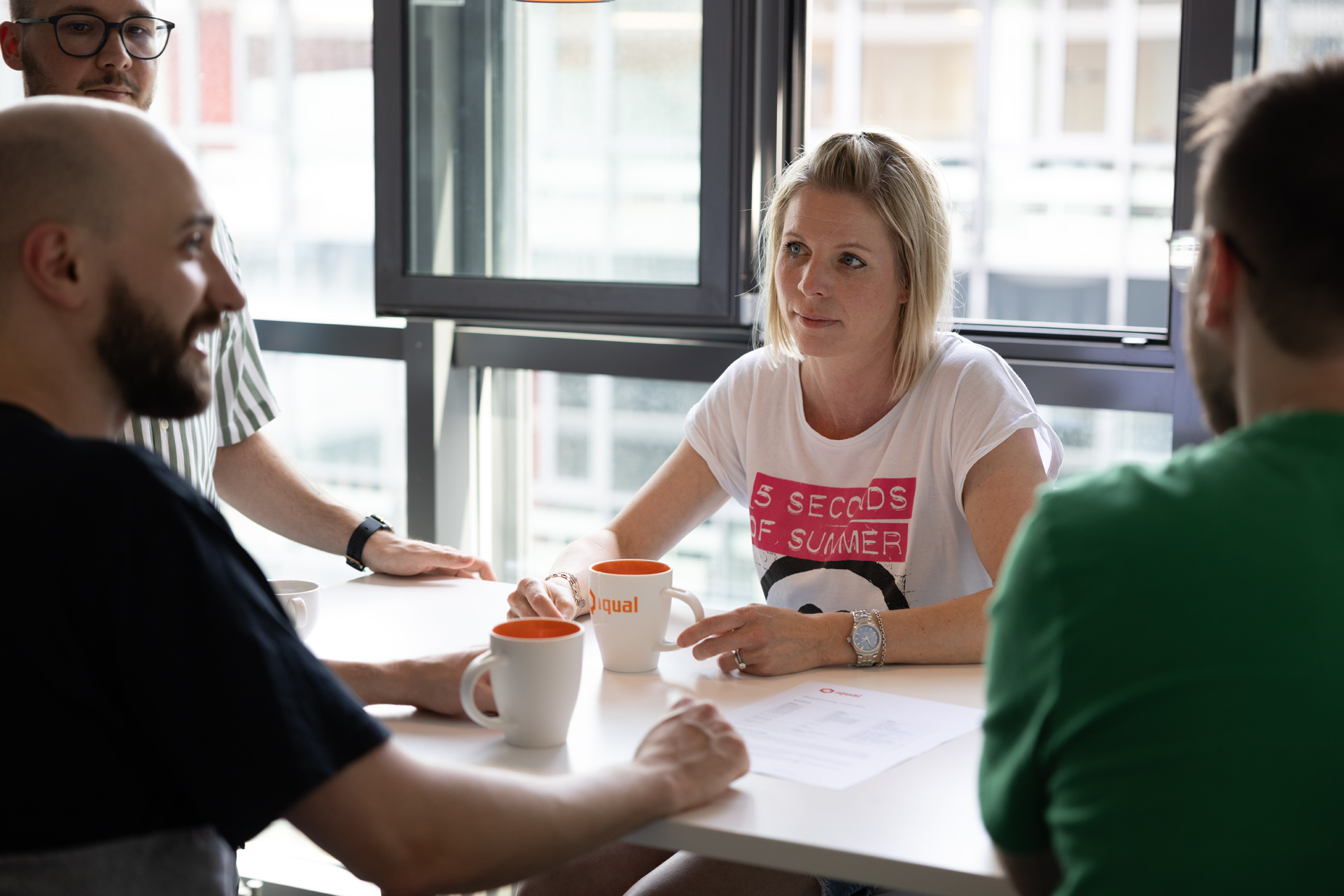 iqual Mitarbeitende hinter einer Kaffeetasse