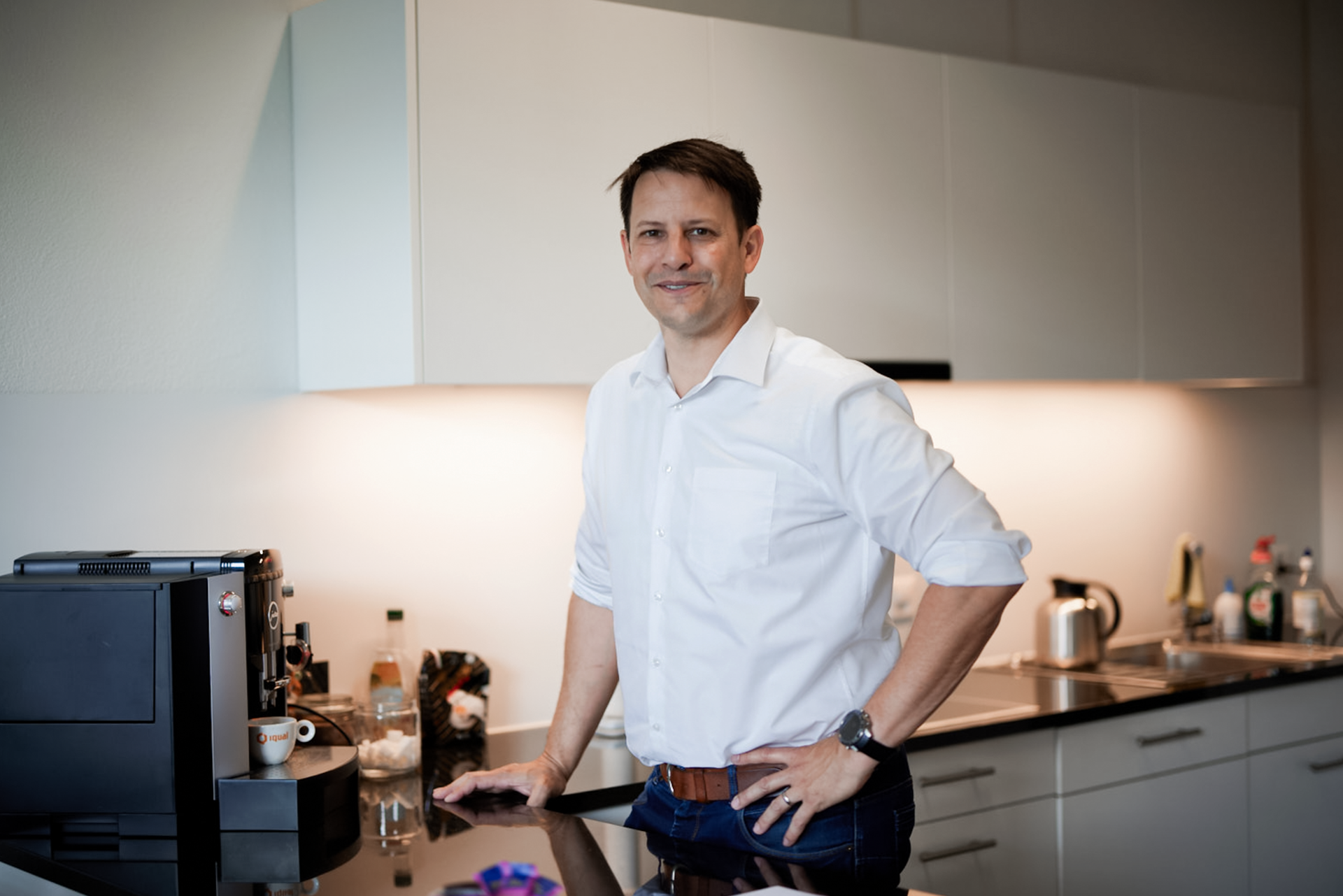 iqual Mitarbeiter steht lächelnd an der Kaffeemaschine iqual Mitarbeiter steht lächelnd an der Kaffeemaschine