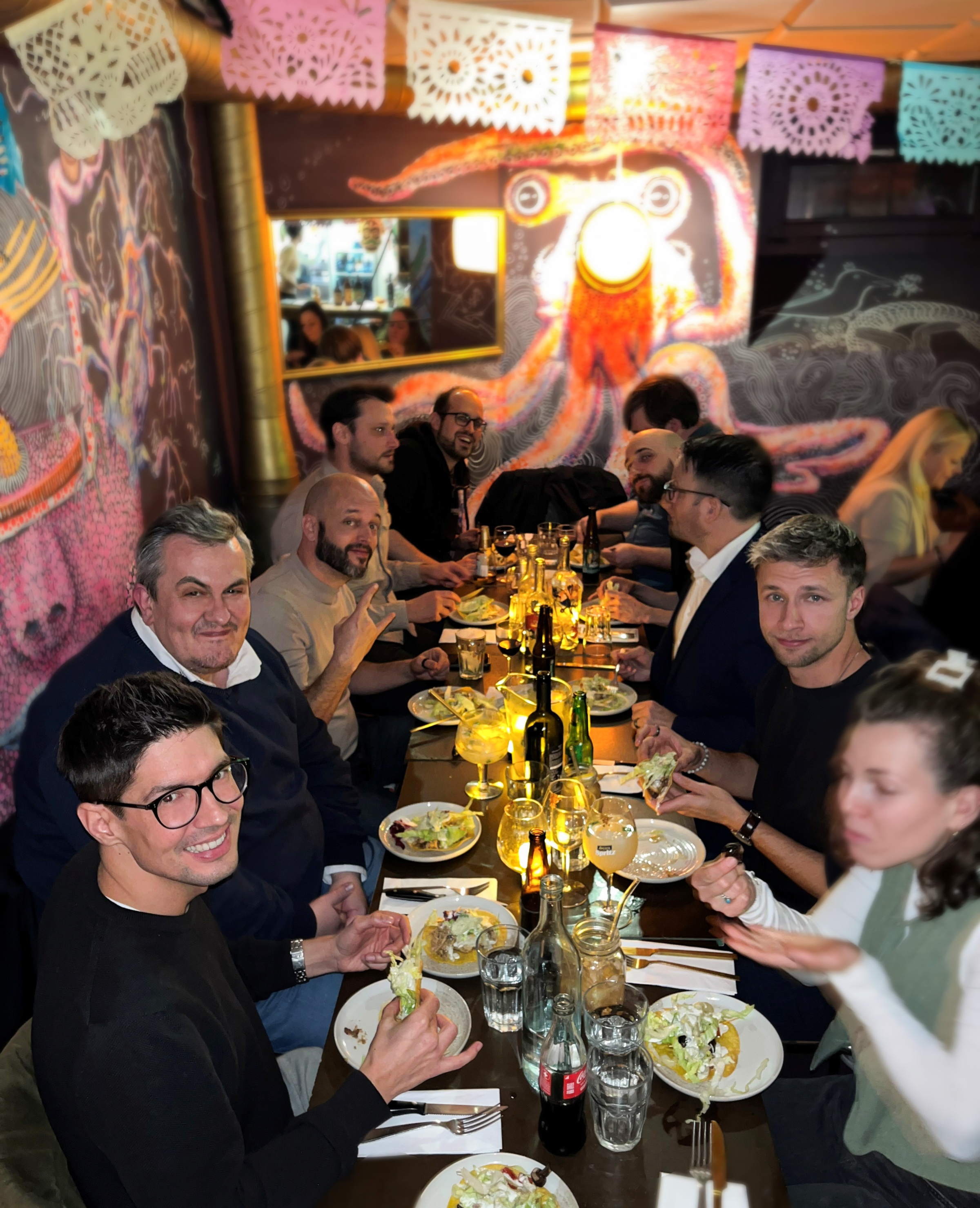 Ein Teil des iqual Teams sitzt lachend an einem Tisch mit geteilten Tellern und Getränken in einem bunten mexikanischen Restaurant in Bern.