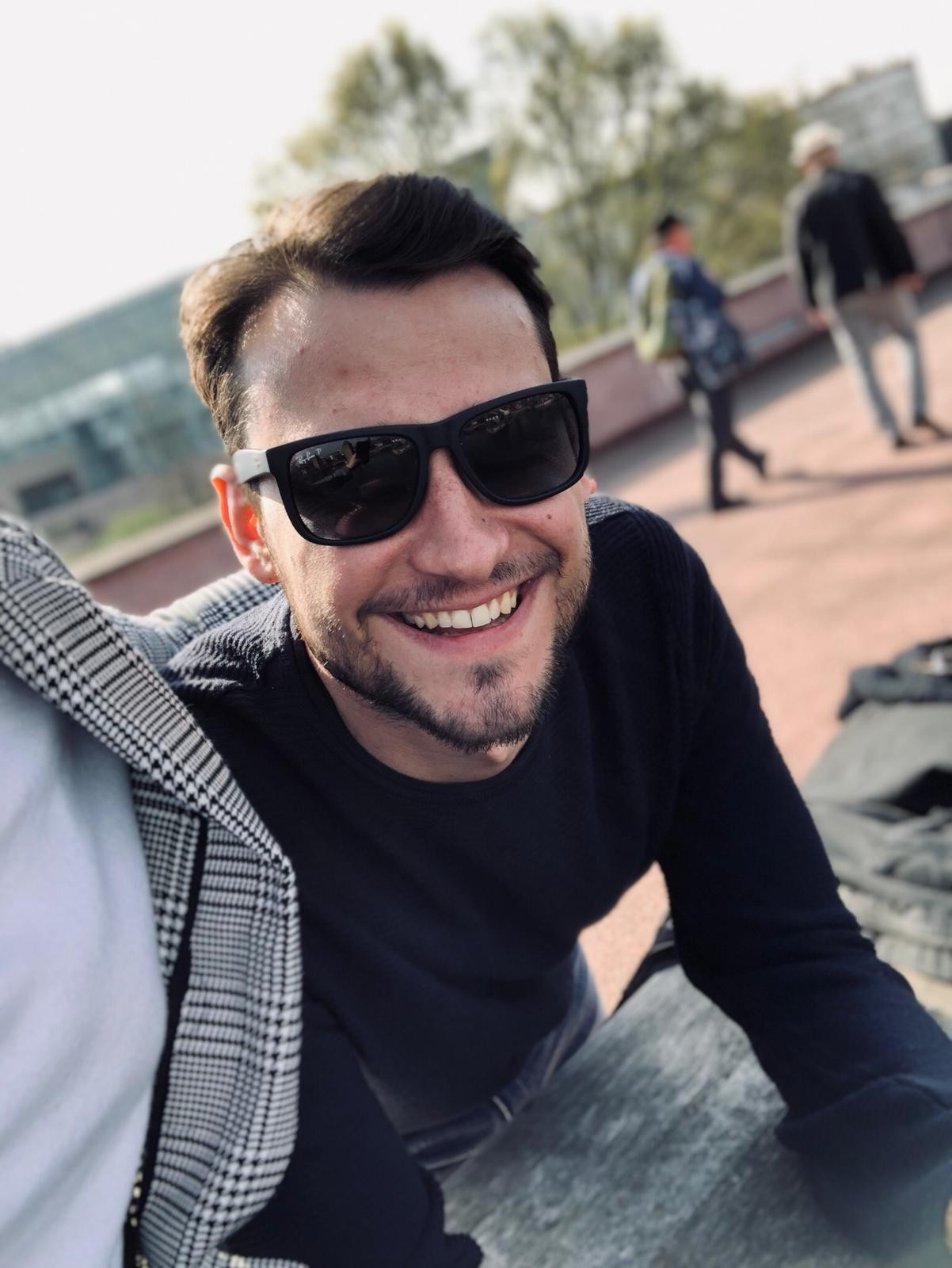 Mitarbeiter Patrick lächelnd mit schwarzer Sonnenbrille an einem warmen, sonnigen Tag